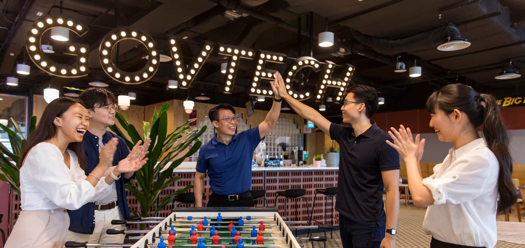Employees working at GovTech bonding over a game of foosball